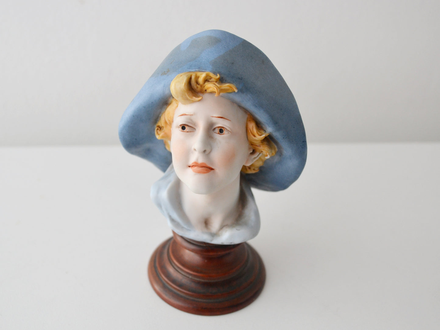 Porcelain bisque bust by Benacchio for Triade, Italy circa 1970s-80s, front view of young woman in blue hat.
