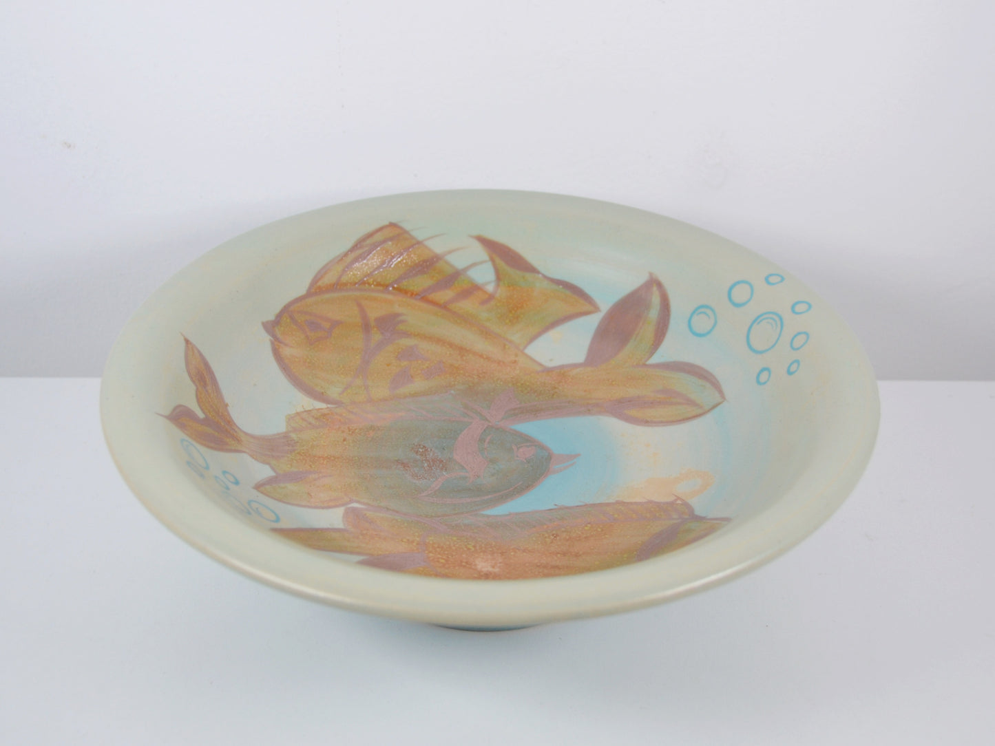 Close-up of hand-painted fish and aquatic plant decoration on Gray's Pottery charger A1017, amber-gold and terracotta tones