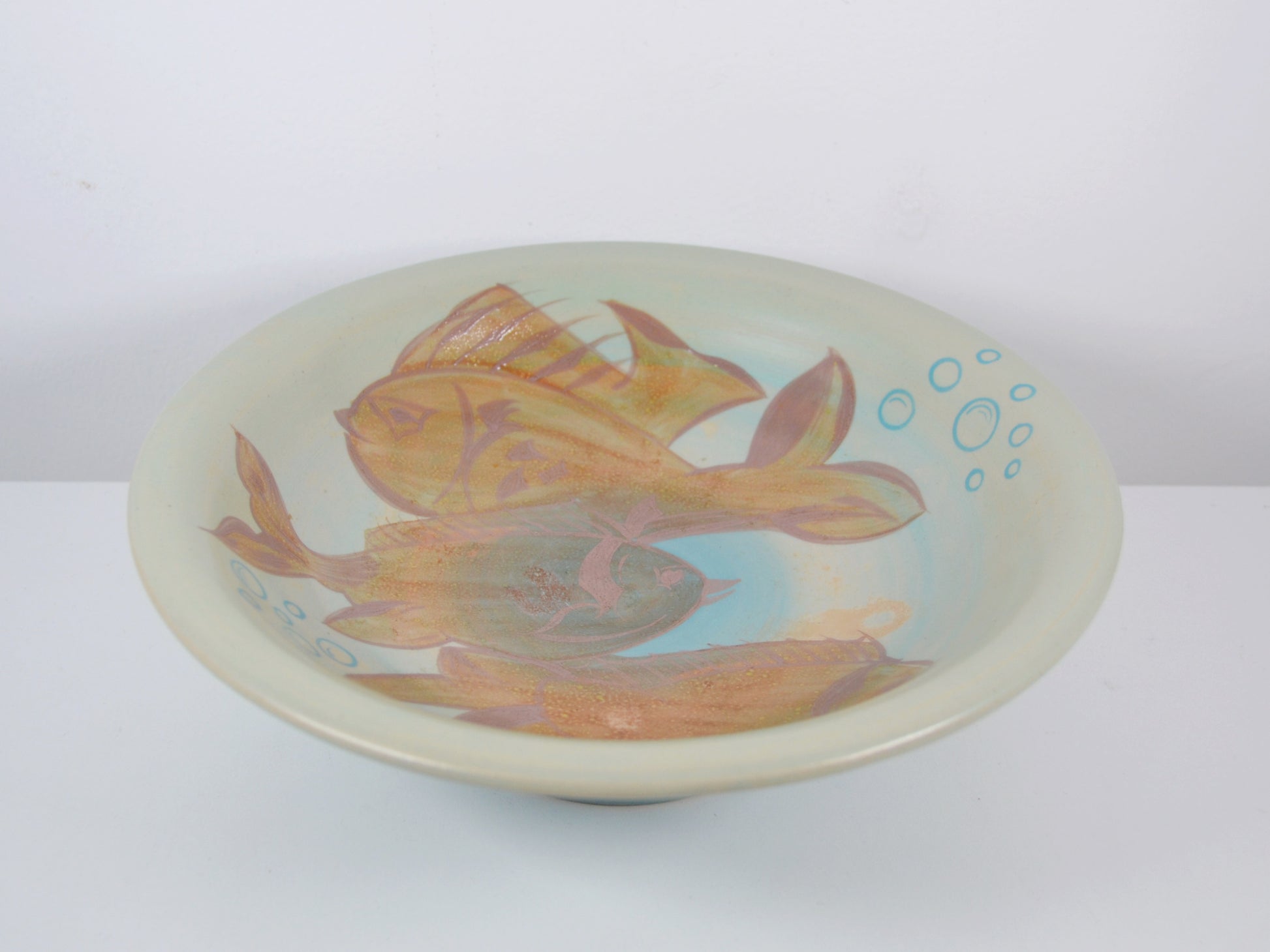 Close-up of hand-painted fish and aquatic plant decoration on Gray's Pottery charger A1017, amber-gold and terracotta tones