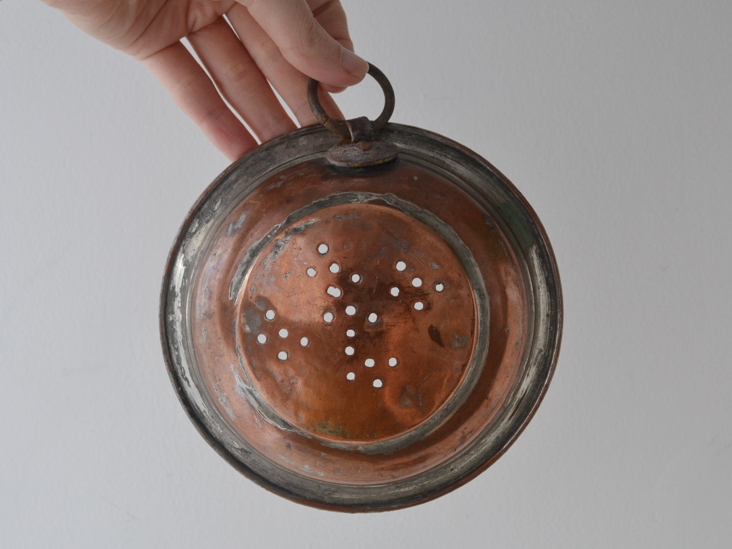 
Antique French copper colander held by ring handle, 19th century, showing pierced star pattern base.