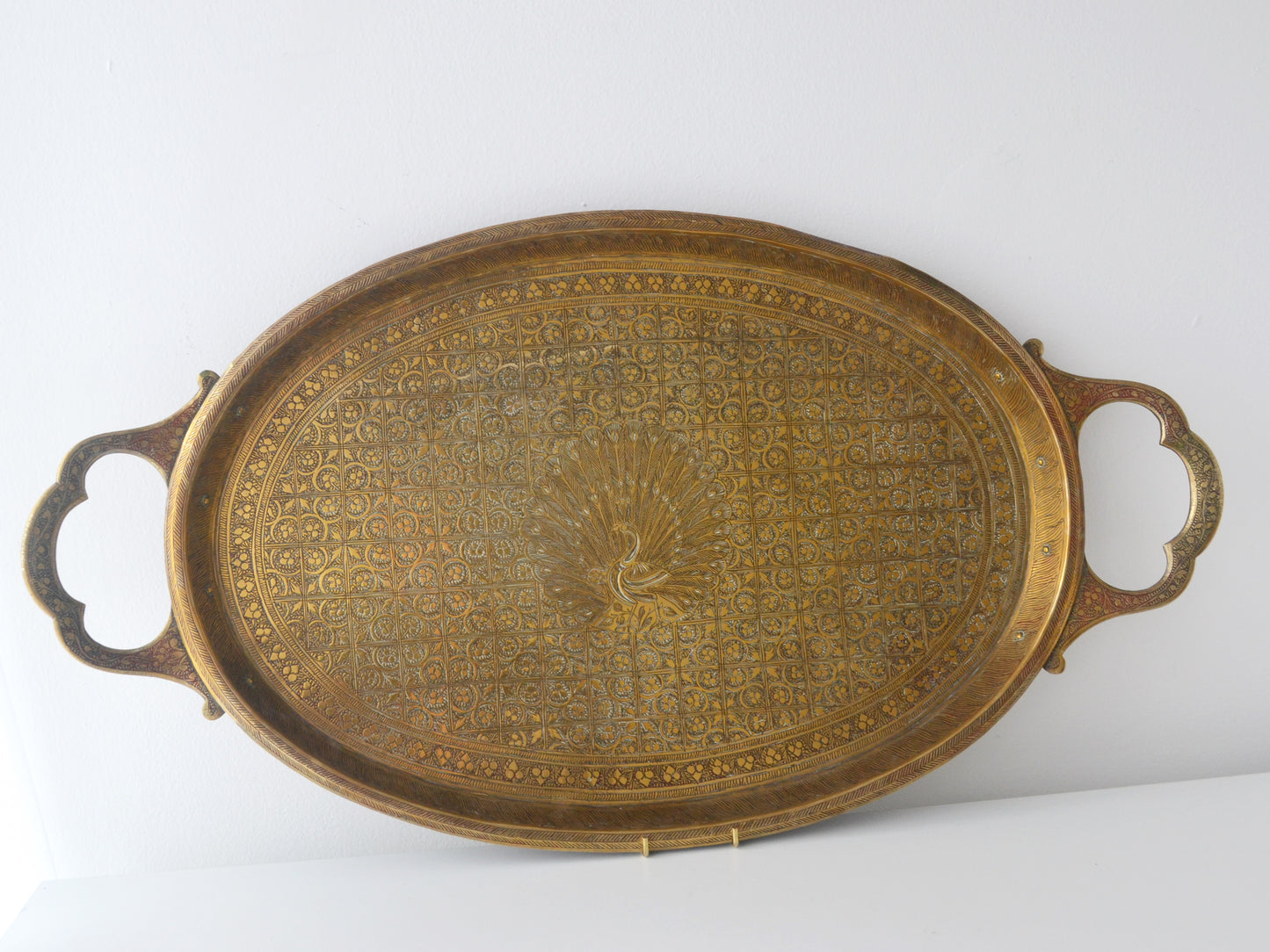 Hand-engraved brass oval tray, central peacock motif, all-over floral grid, India circa 1880–1910, front view