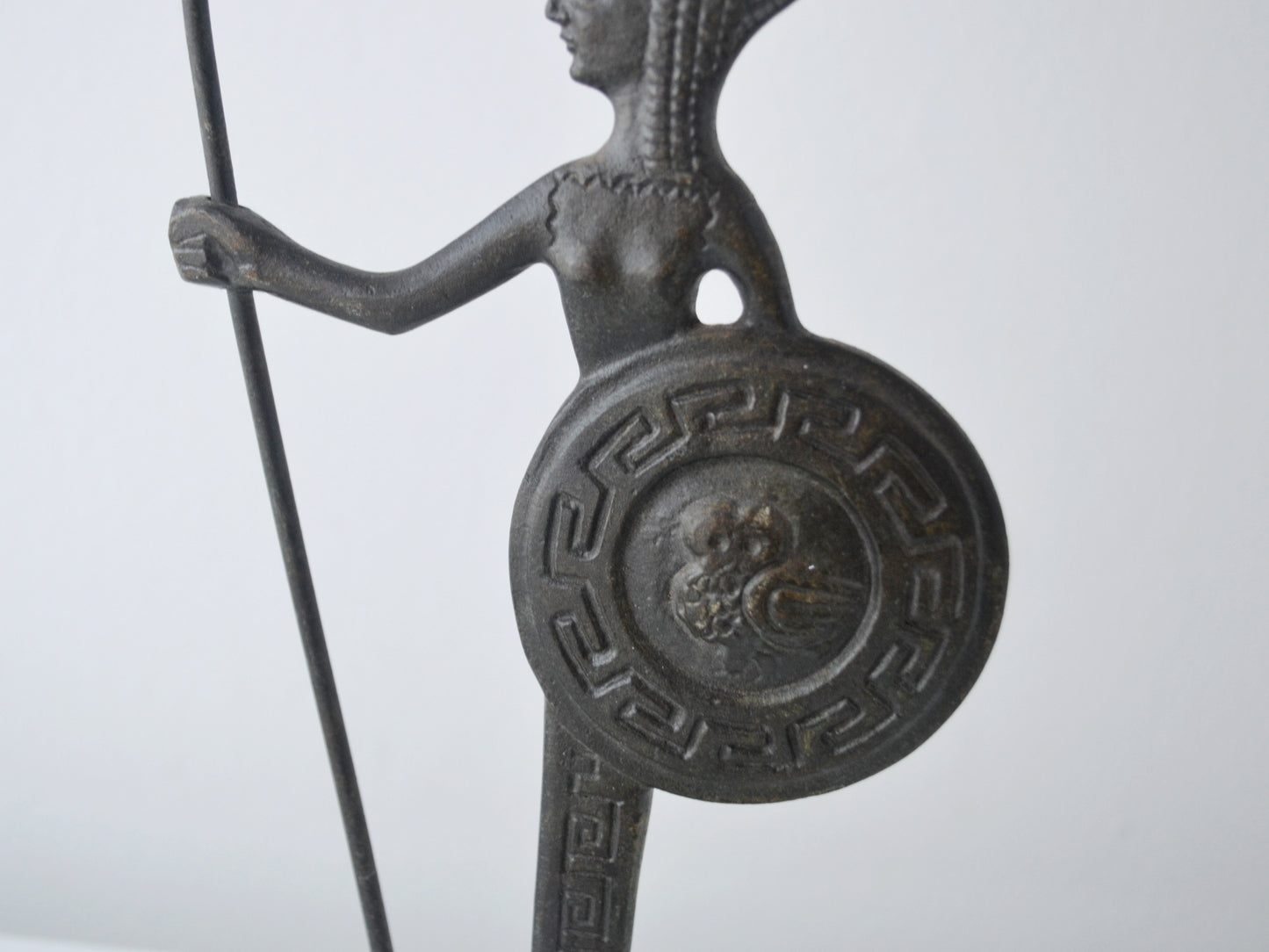 Close-up of owl in relief on shield of vintage Greek bronze Athena figurine, surrounded by meander pattern