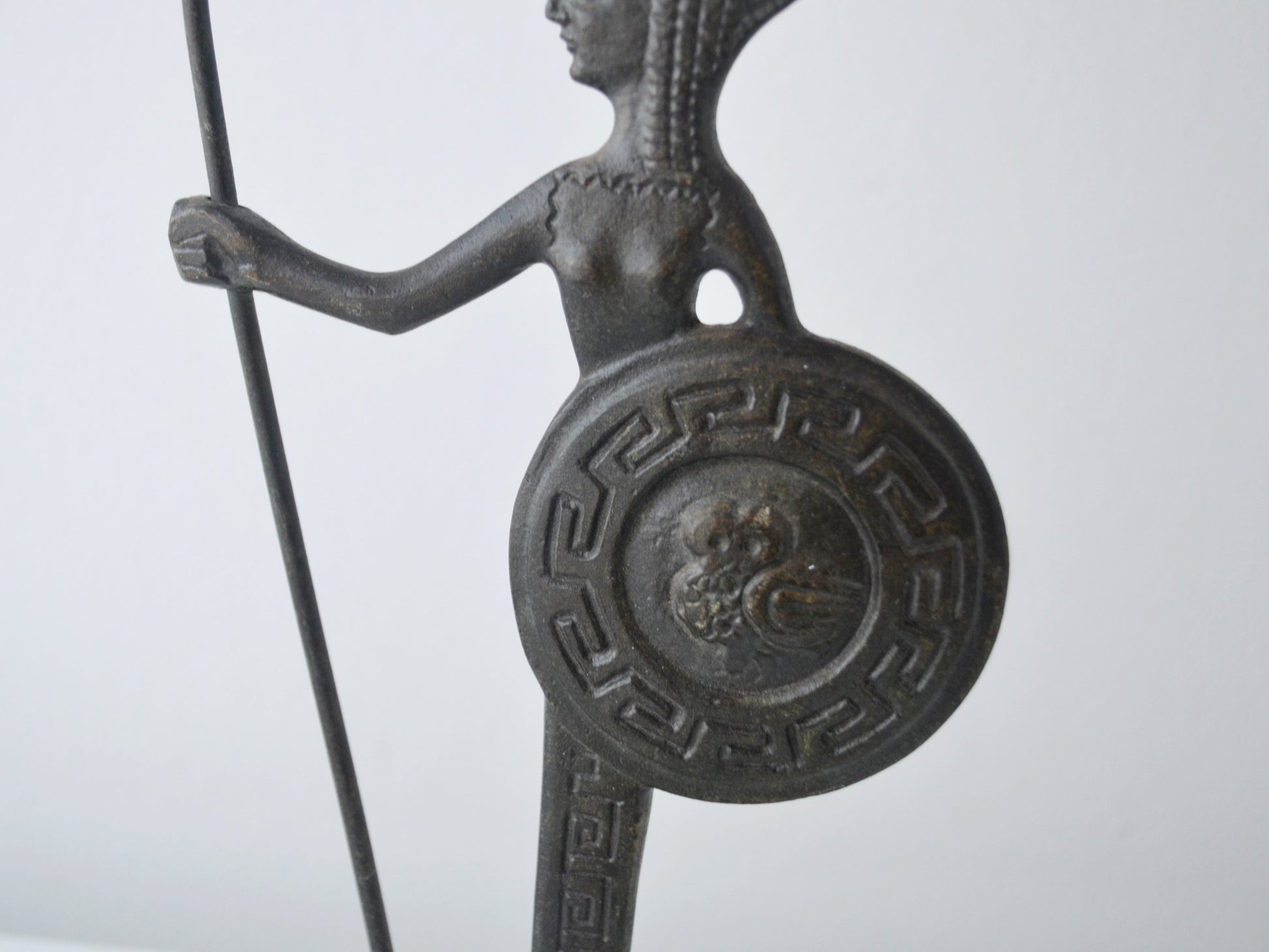 Close-up of owl in relief on shield of vintage Greek bronze Athena figurine, surrounded by meander pattern