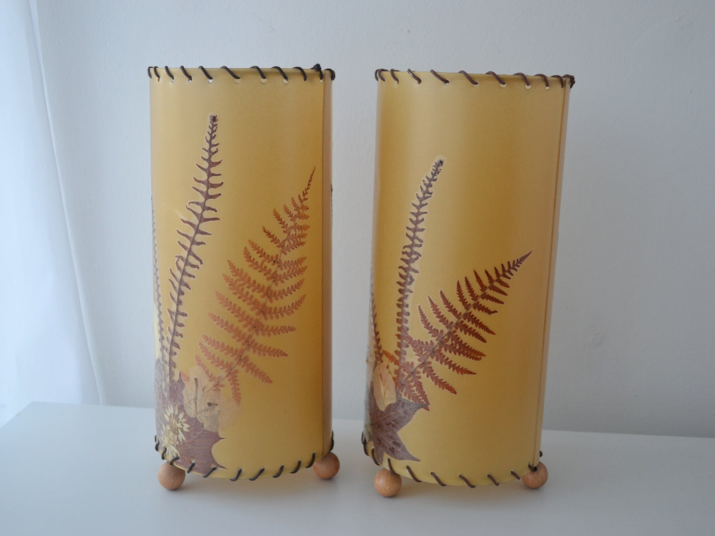 Pressed flower parchment lampshade lit, botanical silhouettes glowing amber, circa 1970s.