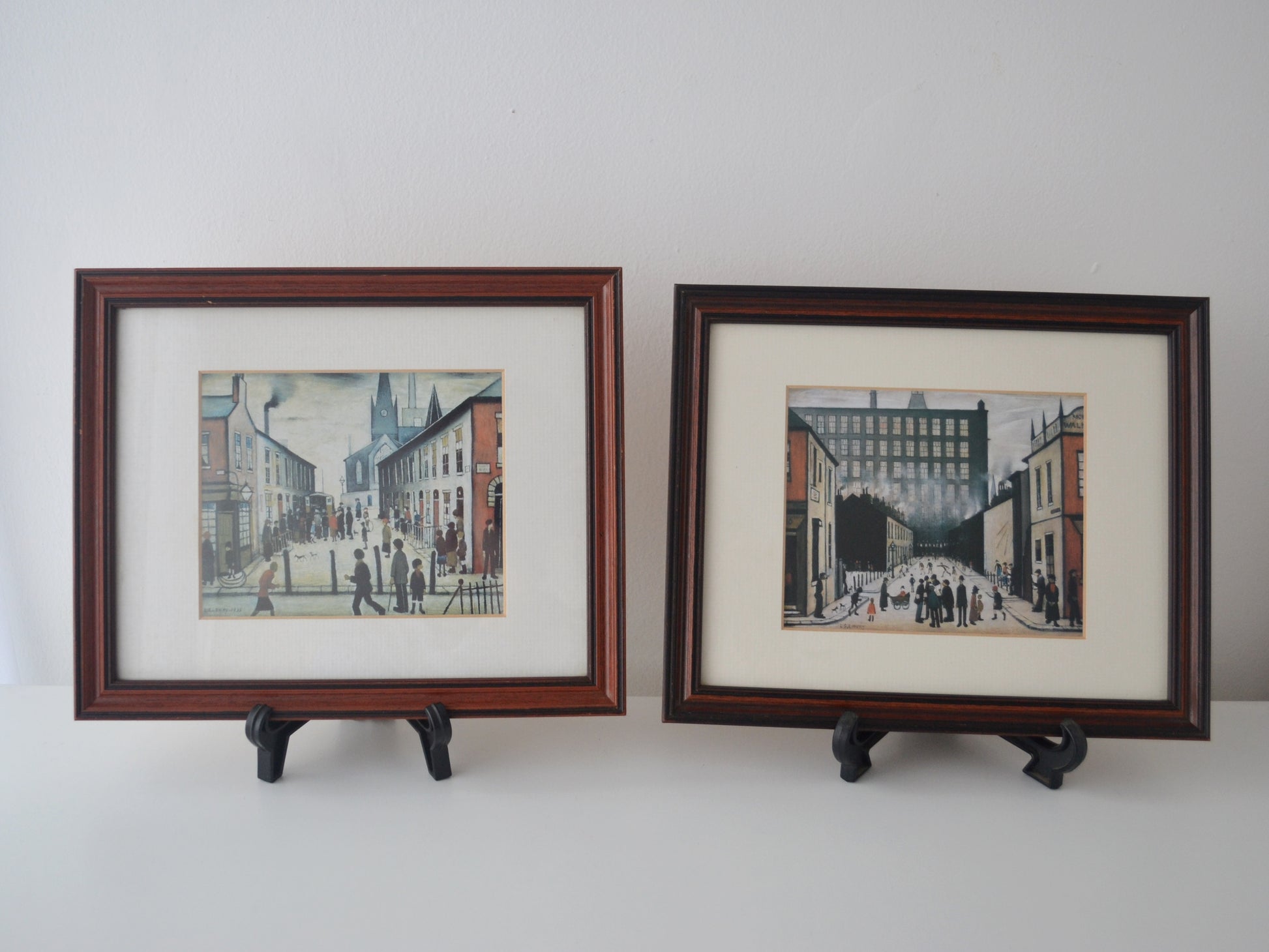 Pair of vintage framed L.S. Lowry colour prints, Fever Van and Street Scene Pendlebury, solid dark wood frames, front view.