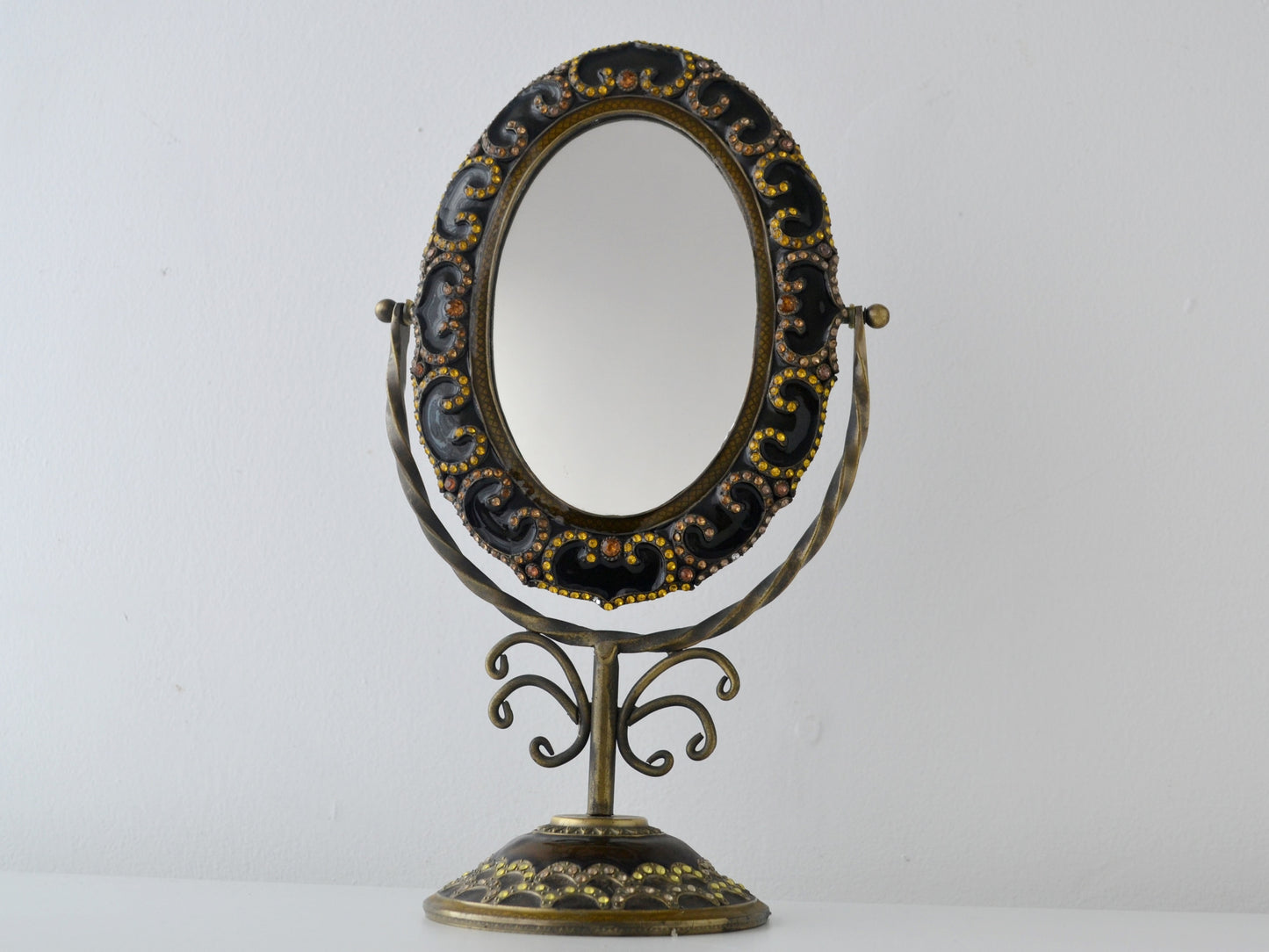 Brass and bronze enamel tilting vanity mirror on scrollwork pedestal stand, rhinestone-set frame, India circa 1960s, front view