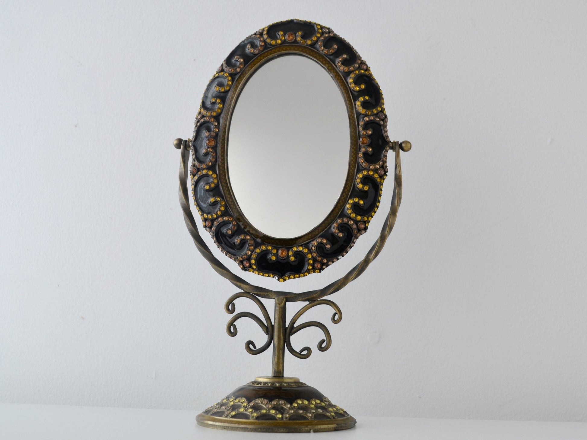 Brass and bronze enamel tilting vanity mirror on scrollwork pedestal stand, rhinestone-set frame, India circa 1960s, front view
