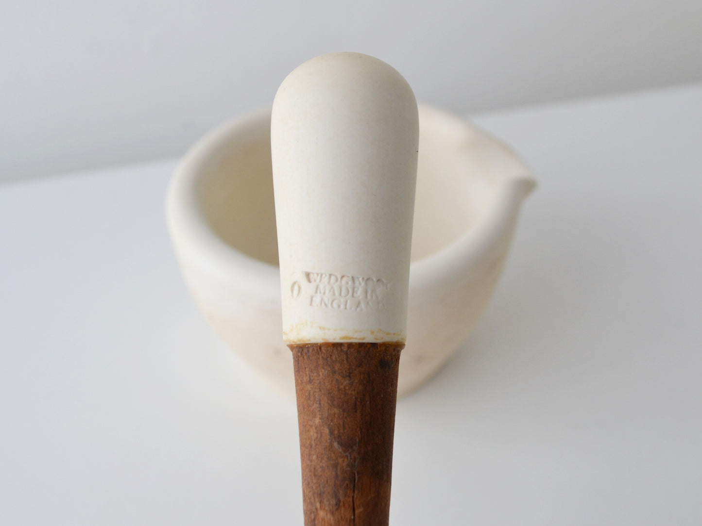 Wedgwood ceramic mortar and pestle set, three-quarter view showing ivory composition body and wooden knop handle, circa 1900