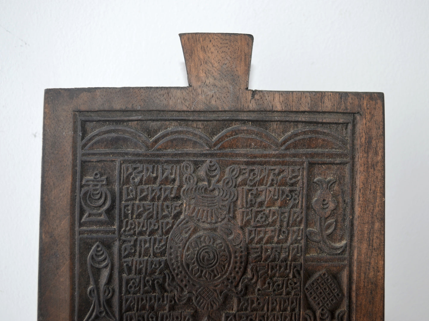 Detail of Tibetan woodblock carving showing Uchen script columns and Ashtamangala border symbols, circa 19th century